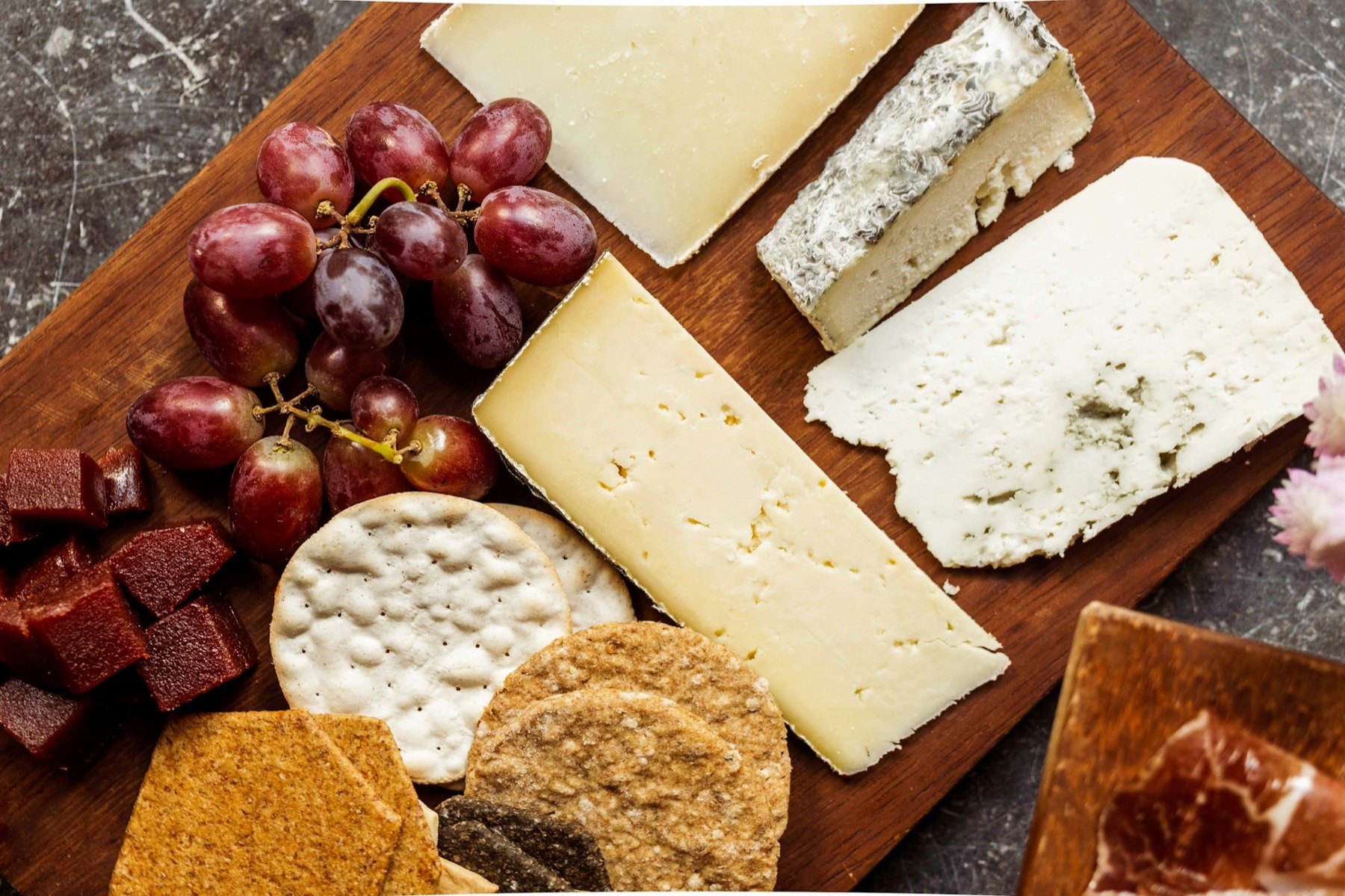 A close, moody composition of cheeses, cured meats, and a glass of red wine on a dark surface.